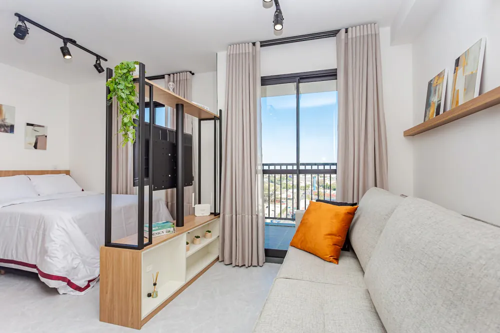 Apartamento central no 13º andar: cama com enxoval de faixa bordô, sofá e janela grande